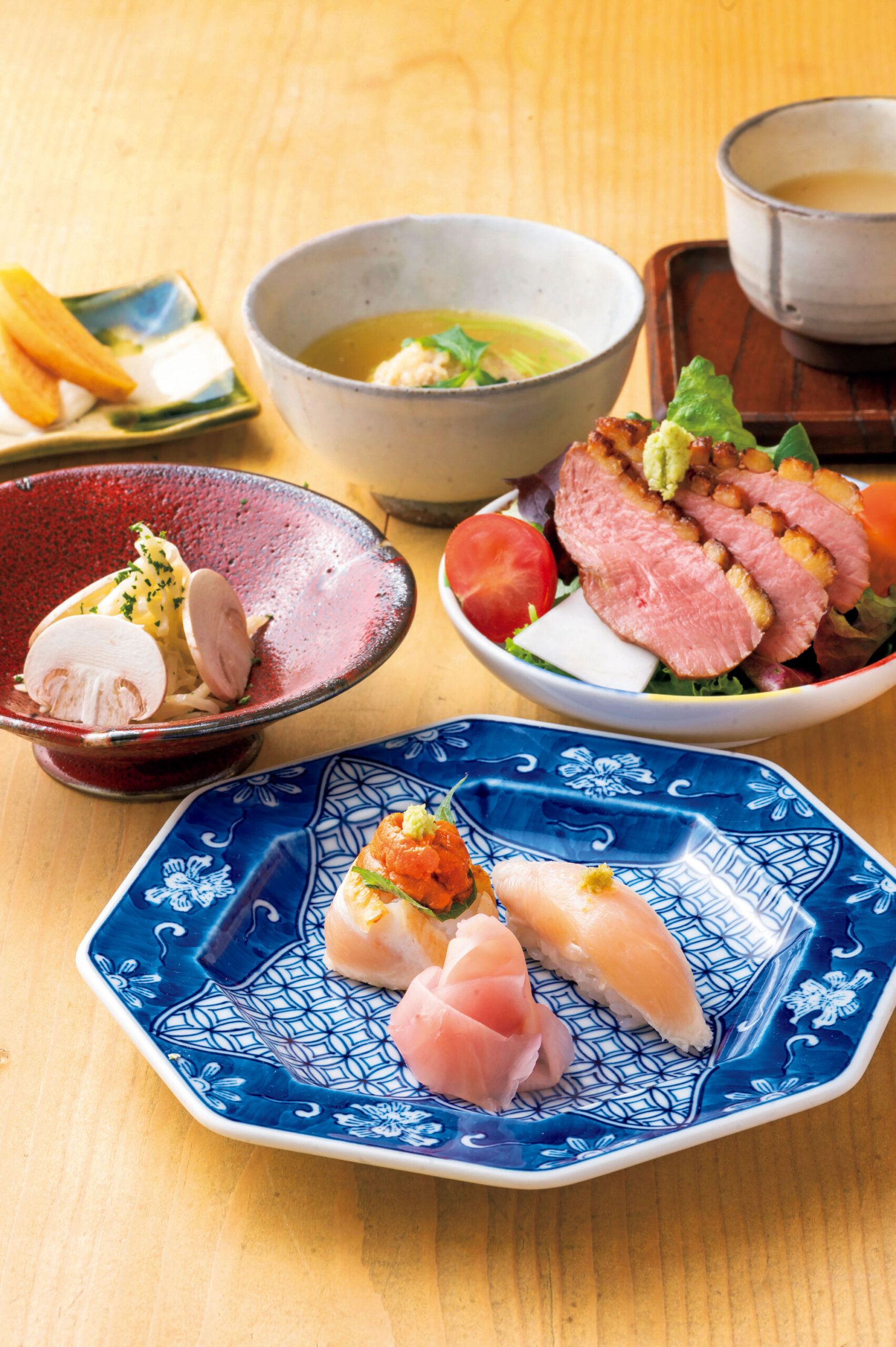 『ヨシモリ』<br />
手前のお皿から時計回りに、鳥のお寿司、小鉢2種、蒸しつくね、スープ、一品<br />
串の途中で供される料理の数々。懐石を意識したコース仕立てだ。最近復活した人気の「鳥のお寿司」はササミの握り＆ムネ肉のたたきとウニの寿司。蒸しつくねは「たて森」から受け継ぐ名物。モモやぼんじりなどを挽いた独自のつくねを生のまま和ダシで蒸す。ほわっとほどける食感