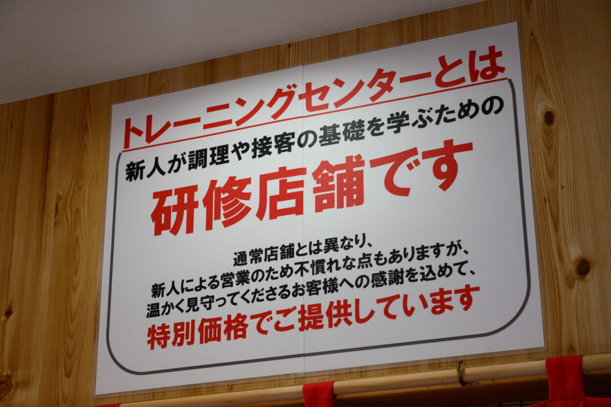 店の壁に貼られた研修店舗であることが書かれた看板。店で奮闘する新人を応援したくなる